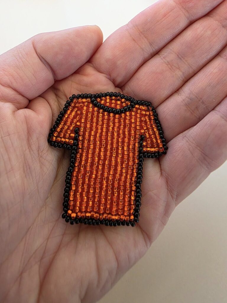 beaded orange shirt pin in the palm of a hand